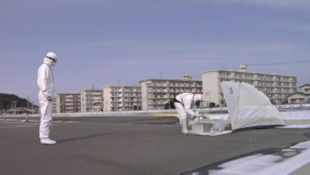 Zwei Personen in Schutzanzügen arbeiten in einem städtischen Gebiet mit wenig Schnee.