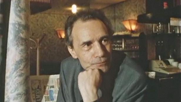 Ein Mann sitzt in einem Café und stützt sein Kinn auf seine Hand.