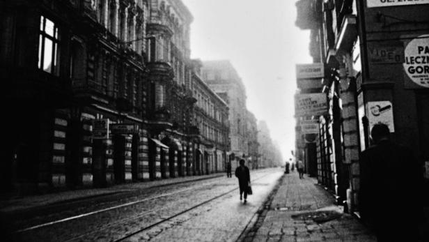 Eine belebte Straße in einer europäischen Stadt mit Menschen und Straßenbahnschienen.