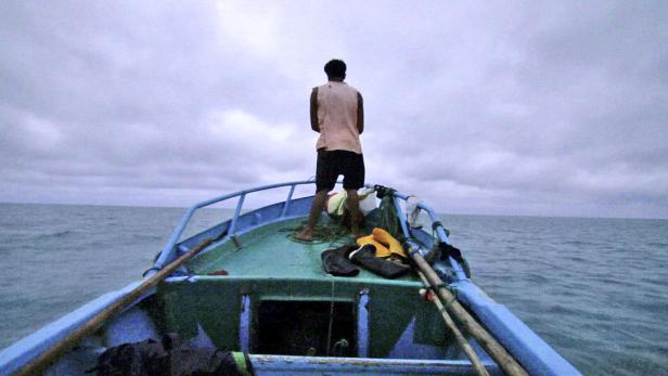 Ein Mann steht auf einem kleinen, blauen Boot auf dem offenen Meer.