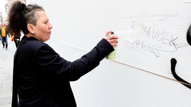 Eine Frau sprüht Graffiti auf eine weiße Wand.