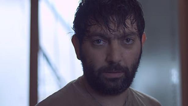 Ein Mann mit Bart und dunklen Haaren blickt in die Kamera.