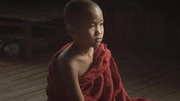Ein junger buddhistischer Mönch sitzt auf dem Boden, im Hintergrund das Filmplakat „Golden Kingdom“.