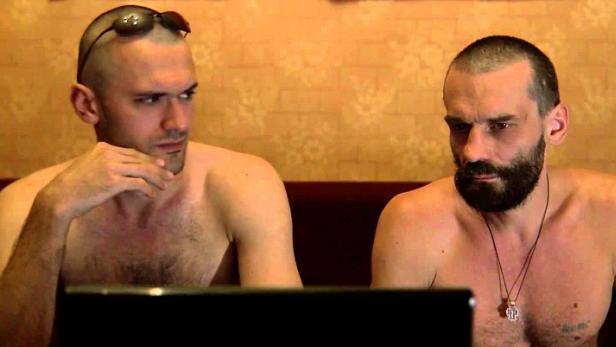 Zwei Männer sitzen mit freiem Oberkörper vor einem Laptop.