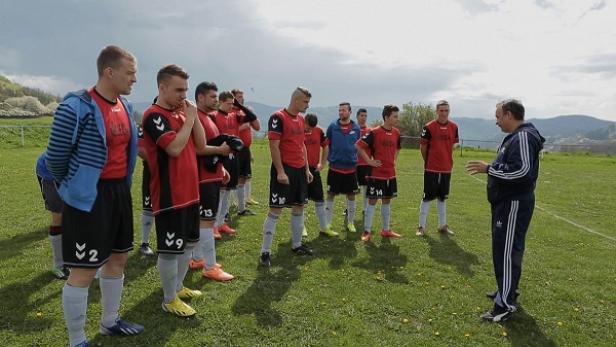 Ein Fußballtrainer bespricht eine Taktik mit seiner Mannschaft auf dem Spielfeld.