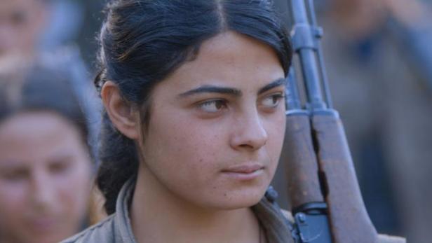 Eine junge Frau mit einem Gewehr über der Schulter blickt entschlossen zur Seite.