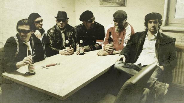 Eine Gruppe von sechs Männern sitzt an einem Tisch und trinkt Bier.