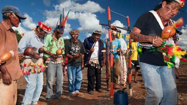 Eine Gruppe indigener Männer hält Kürbisse und trägt traditionelle Kopfbedeckungen.