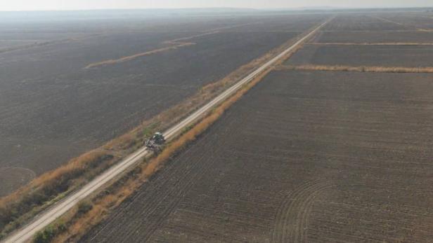 Ein Traktor fährt auf einem Feldweg durch eine weite, braune Ackerlandschaft.