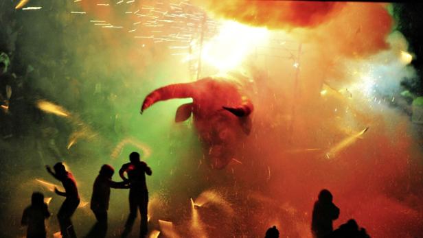 Menschen nehmen an einem Correfoc-Feuerlauf mit einem Stierkopf teil.