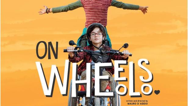 Ein Junge im Rollstuhl fährt ein Motorrad, während ein Mädchen hinter ihm steht, Filmposter „On Wheels“.