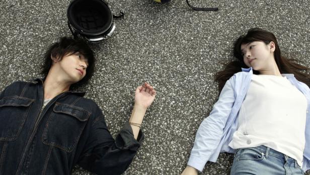 Ein junges Paar liegt auf dem Asphalt, ein Motorradhelm daneben.