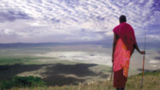 Ein Massai steht auf einem Hügel und blickt auf eine weite Landschaft.