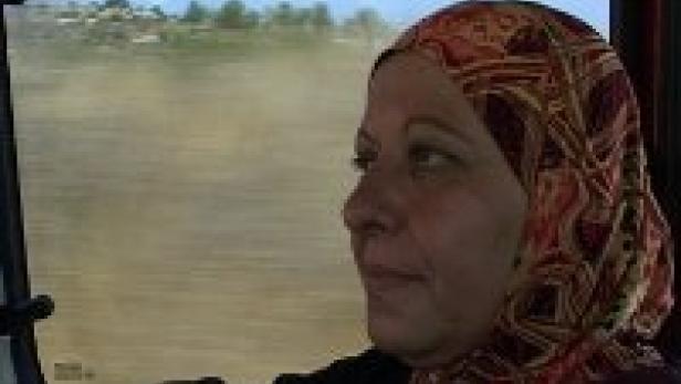 Eine Frau mit Kopftuch schaut aus dem Fenster eines fahrenden Fahrzeugs.