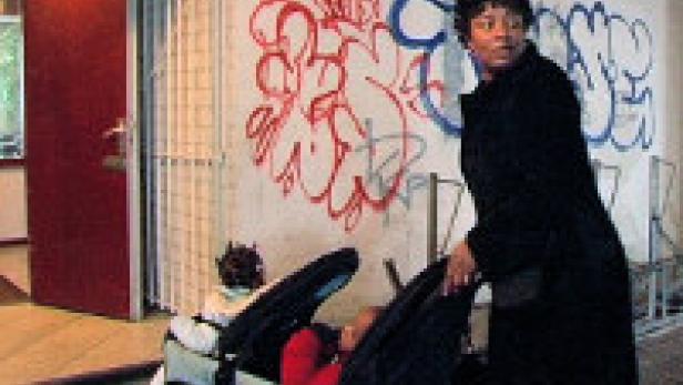 Eine Frau schiebt einen Kinderwagen vor einer Wand mit Graffiti.