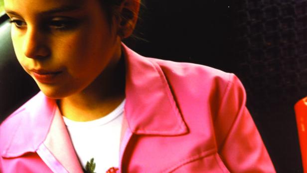 Ein junges Mädchen mit rosa Jacke schaut nachdenklich zur Seite.