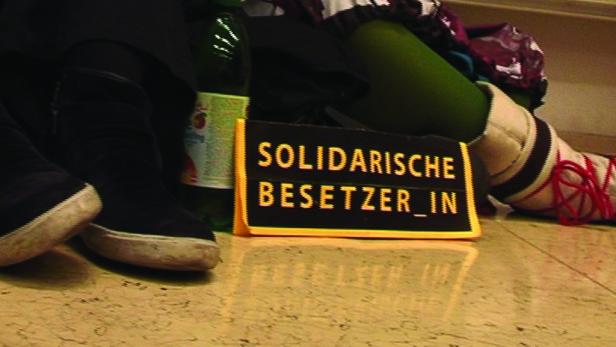Ein Schild mit der Aufschrift „Solidarische Besetzer_in“ steht auf dem Boden.