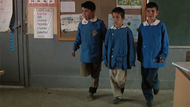 Drei Jungen in Schuluniformen gehen in einem Klassenzimmer entlang.