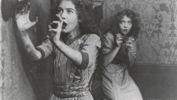 Zwei junge Frauen, eine mit einem Rohrlauscher, wirken erschrocken.