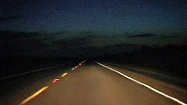 Eine dunkle Landstraße in der Nacht mit gelben und weißen Fahrbahnmarkierungen.