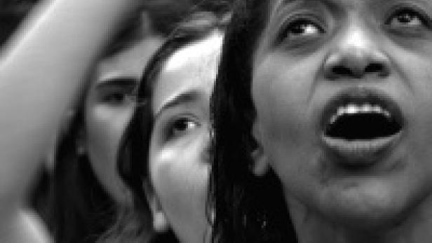 Eine Frau schreit mit geöffnetem Mund, während andere Frauen im Hintergrund zu sehen sind.