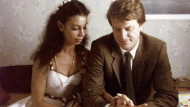 Ein Mann im Anzug und eine Frau im weißen Kleid sitzen nebeneinander.