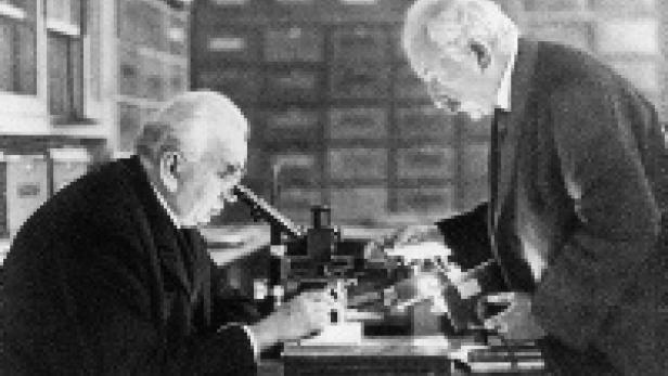 Zwei ältere Männer beugen sich über ein Mikroskop in einem Labor.