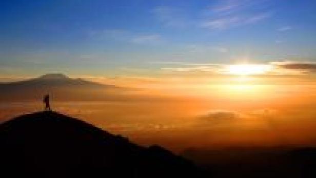 Eine Person steht auf einem Hügel und blickt auf den Sonnenaufgang über den Wolken.