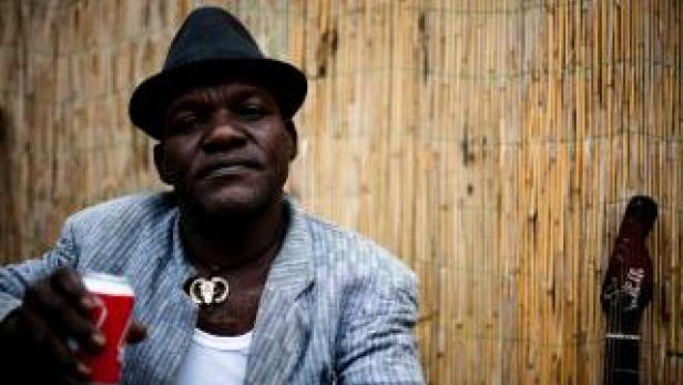 Ein Mann mit Hut hält eine Dose in der Hand, neben ihm eine Gitarre.