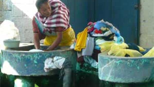 Eine Frau wäscht Kleidung in einem Waschbecken im Freien.