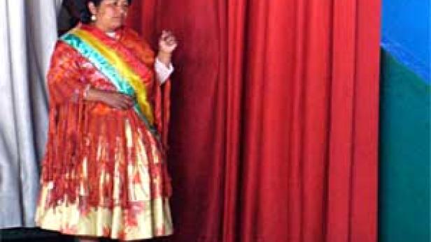 Eine Frau in traditioneller Kleidung und Hut steht vor roten Vorhängen.