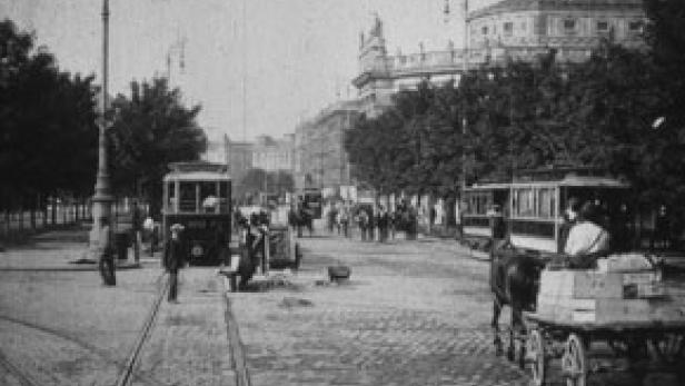 Eine belebte Straße mit Straßenbahnen und Pferdekutschen in einer Stadt um die Jahrhundertwende.