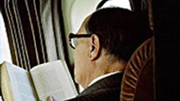 Ein Mann mit Brille liest ein Buch im Flugzeug.