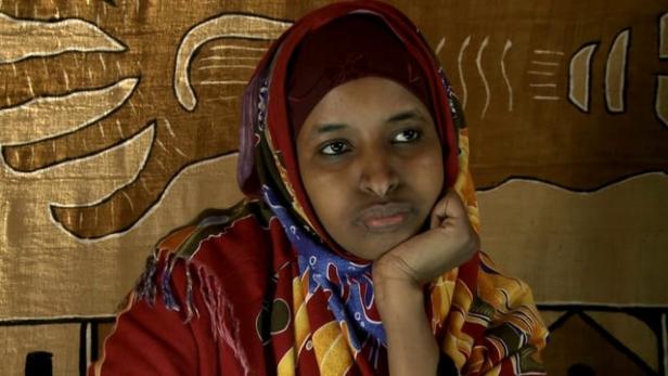 Eine Frau mit Kopftuch und gemustertem Schal stützt ihr Kinn auf ihre Hand.