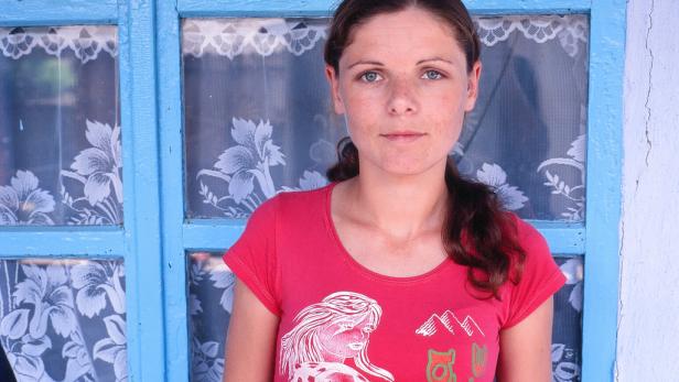 Eine junge Frau mit roten T-Shirt steht vor einem blau gestrichenen Fenster.