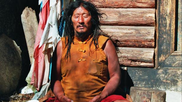 Ein Mann mit Dreadlocks meditiert vor einer Holzwand.