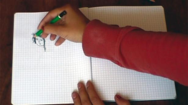 Eine Person zeichnet mit einem grünen Stift ein Gesicht in ein Notizbuch.