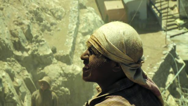 Ein Mann mit Kopftuch steht vor einer staubigen Felswand.