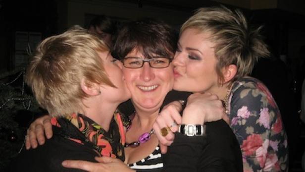 Zwei Frauen geben einer Frau mit Brille einen Kuss auf die Wange.