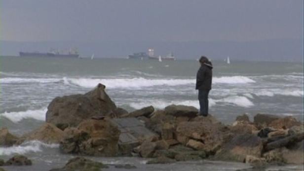 Eine Person steht auf Felsen am Ufer und blickt auf das stürmische Meer.