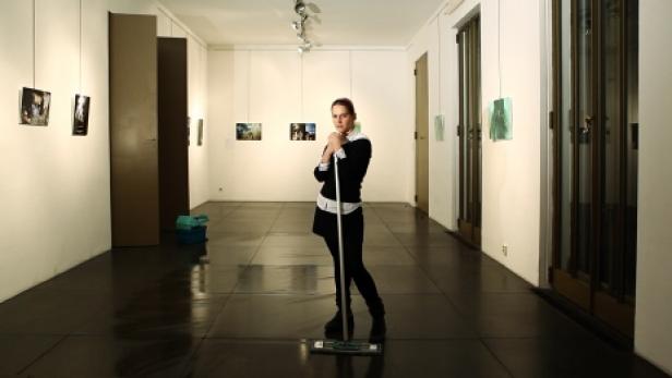 Eine Frau lehnt an einem Mopp in einem langen Flur mit Kunst an den Wänden.