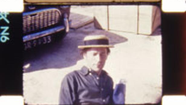 Ein Mann mit Hut steht vor einem Auto, aufgenommen auf einem Filmstreifen.