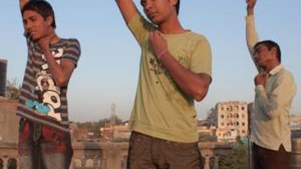 Drei junge Männer stehen auf einem Dach und heben die Arme.