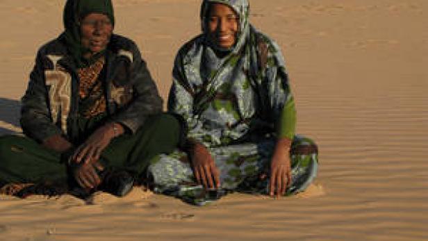 Zwei Frauen sitzen in traditioneller Kleidung in einer Wüste.