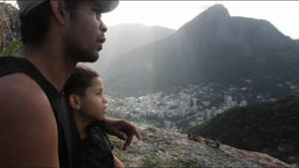Ein Mann und ein Kind blicken auf eine Stadt in einem Tal mit einem Berg im Hintergrund.