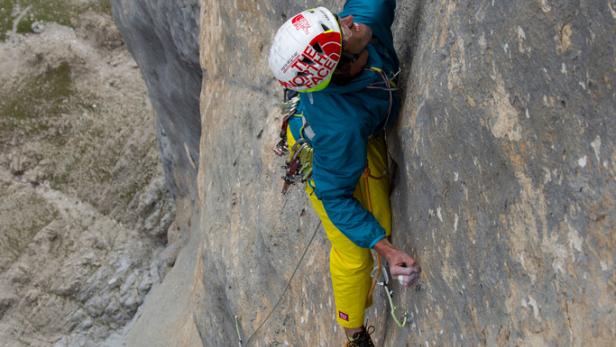 Ein Kletterer hängt an einer steilen Felswand, gesichert durch ein Seil.
