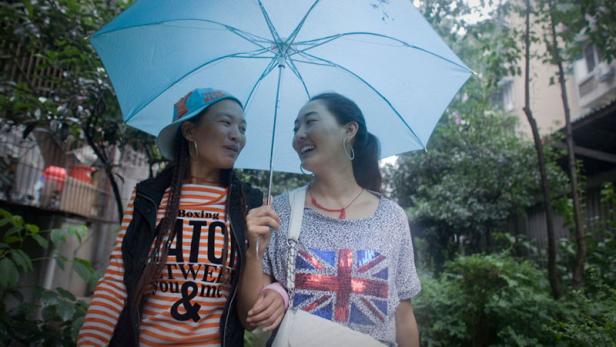 Zwei Frauen stehen unter einem blauen Regenschirm und lächeln sich an.
