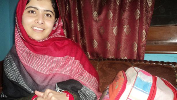 Malala Yousafzai lächelt mit einem roten und schwarzen Schal in die Kamera.