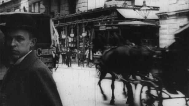 Eine belebte Straße mit einer Pferdekutsche und Passanten in einer historischen Aufnahme.