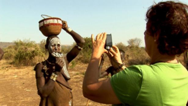 Eine Touristin fotografiert eine Frau vom Stamm der Mursi mit Lippenteller in Äthiopien.